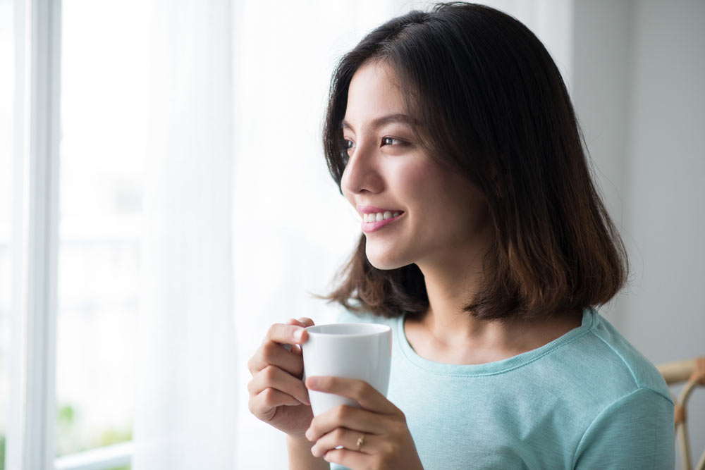 woman sitting at opened window drinking coffee